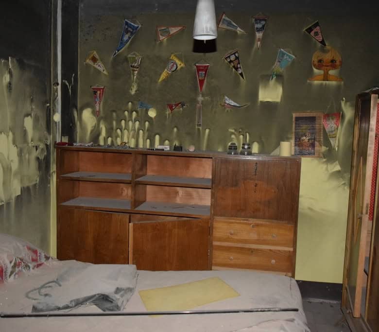 Abandoned bedroom showing damaged walls, worn furniture, and cluttered space in Baza, Granada.