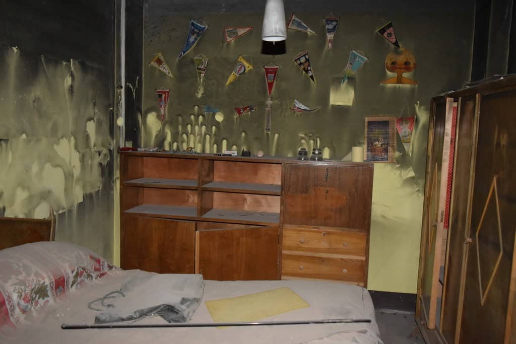 Abandoned bedroom showing damaged walls, worn furniture, and cluttered space in Baza, Granada.