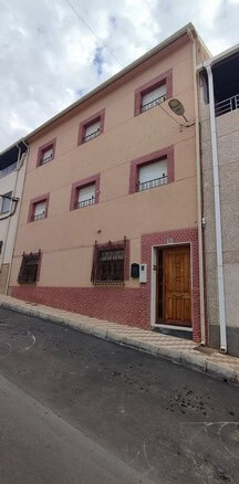 Town house in Tijola, Almeria with a wooden front door and small windows, situated on a quiet street.