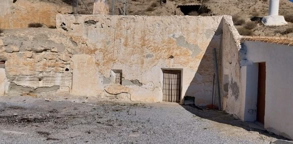 Cave house in Cantarranas, Granada, with rustic stone walls and simple wooden door.