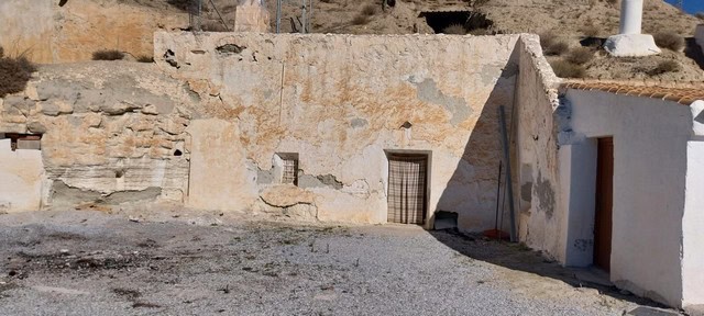 Cave house in Cantarranas, Granada, with rustic stone walls and simple wooden door.