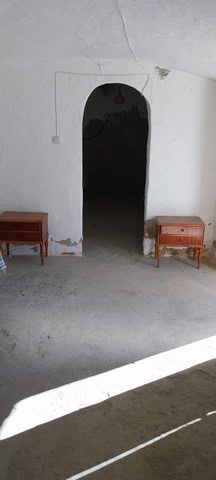 Cave house entrance in Cantarranas, Granada with white walls and rustic furniture.