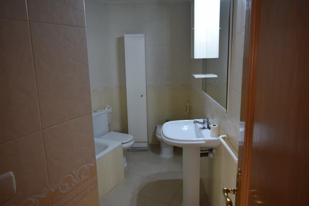 Bathroom in an apartment located in Baza, Granada, featuring a toilet, sink, and mirror.