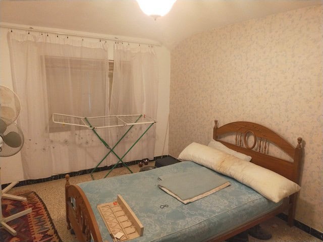 Comfortable bedroom with wooden bed frame and natural light in Los Olivos, Granada.