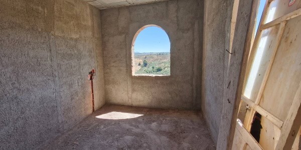 Village property in Fontanar, Jaen with unfinished interior and scenic view through arched window.
