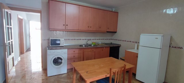 Kitchen with wooden cabinets, fridge, washing machine, and dining table in Purchena village property.