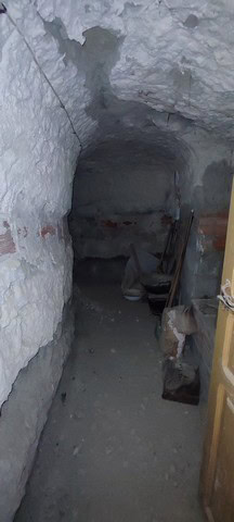 Interior view of a cave house in La Alqueria, Granada, showing rough stone walls and basic furnishin.