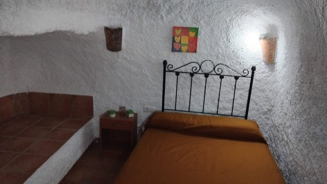 Unique cave house interior in Cantarranas, Granada with rustic walls and cozy bedroom.