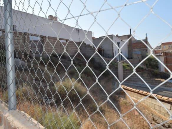 Cave house in Caniles, Granada, with surrounding fencing and hillside terrain.