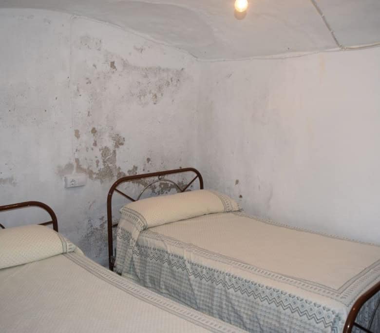 Interior view of a rustic cave house bedroom in Caniles, Granada, featuring two beds and simple deco.