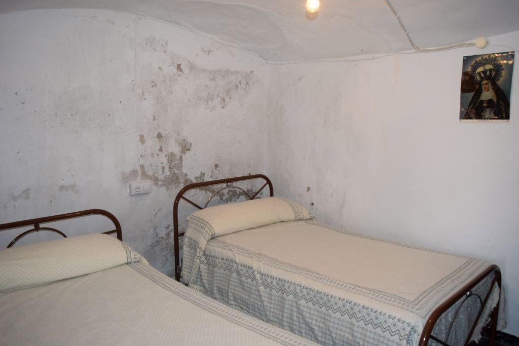 Interior view of a rustic cave house bedroom in Caniles, Granada, featuring two beds and simple deco.