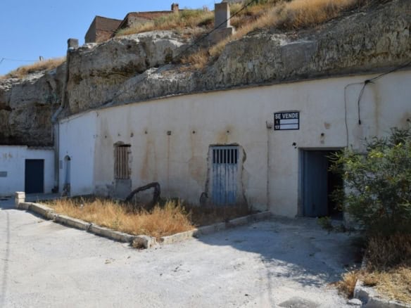 Cave house exterior in Caniles, Granada, with rustic doors and a "For Sale" sign.