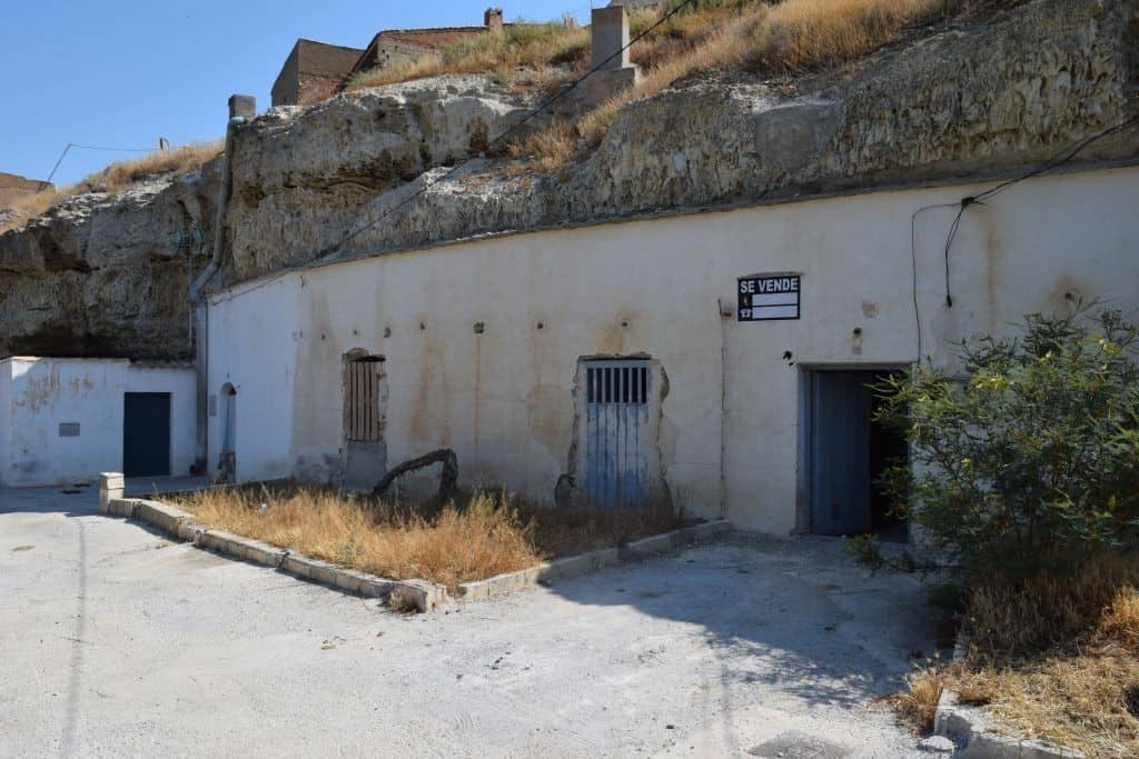 Cave house exterior in Caniles, Granada, with rustic doors and a "For Sale" sign.