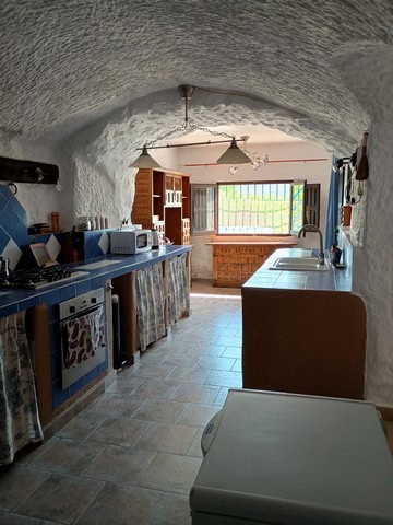 Cave house interior with rustic kitchen, wooden shelves, and natural stone walls in Cortes de Baza,.