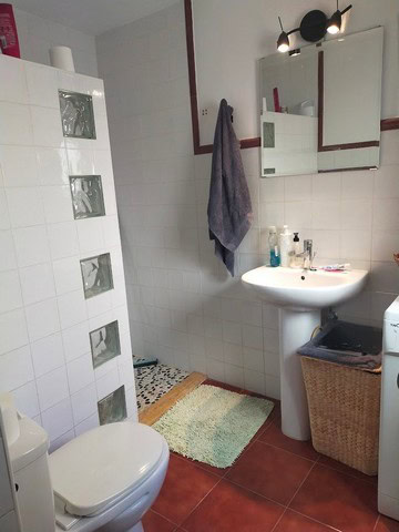 Bathroom with white tiles, sink, mirror, and laundry area in Urracal village property.