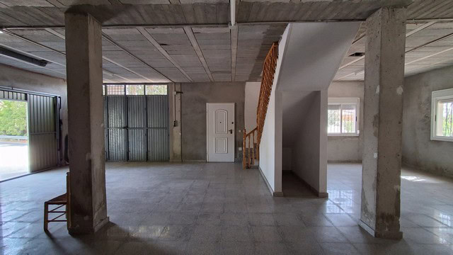 Interior view of a spacious, unfinished rural property with concrete pillars and large windows.