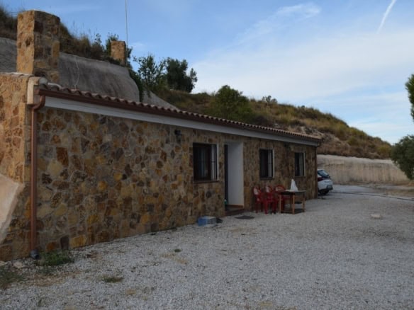Cave house with stone exterior in Cuevas del Campo, Granada, surrounded by natural landscape.