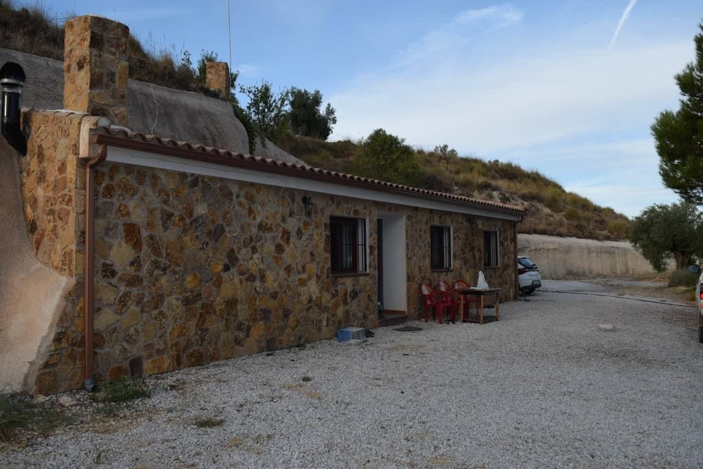 Cave house with stone exterior in Cuevas del Campo, Granada, surrounded by natural landscape.
