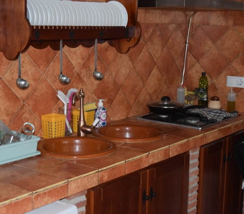 Cave house kitchen with rustic terracotta tiles, dual sinks, and basic appliances in Cuevas del Camp.