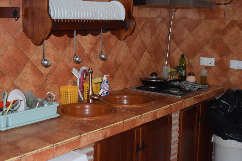 Cave house kitchen with rustic terracotta tiles, dual sinks, and basic appliances in Cuevas del Camp.
