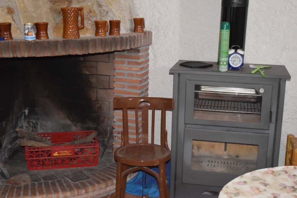 Cave house interior with fireplace, wooden chair, and stove in Cuevas del Campo, Granada.