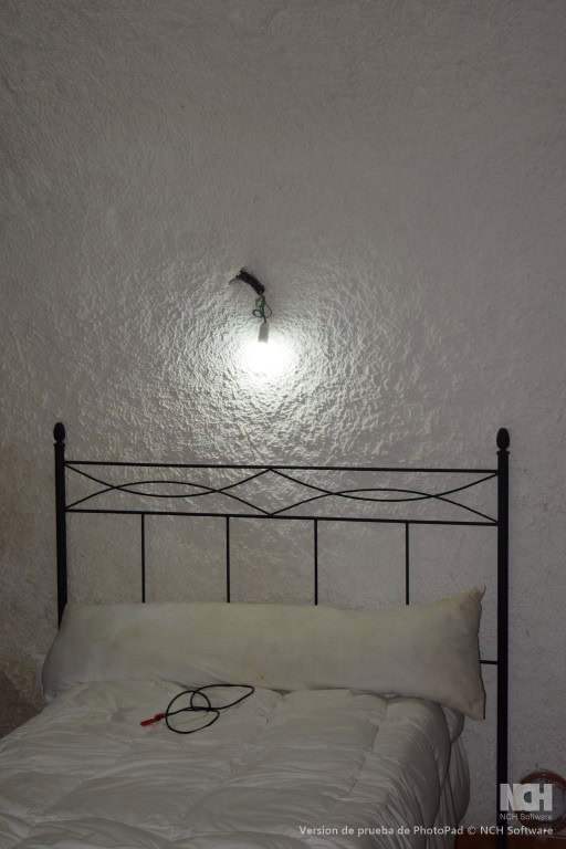 Interior of a cave house bedroom in Cuevas del Campo, Granada with a simple bed and wall-mounted lig.