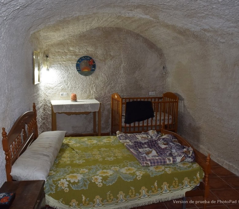 Cave house interior with rustic wooden bed, cozy decor, and arched ceiling in Cuevas del Campo, Gran.