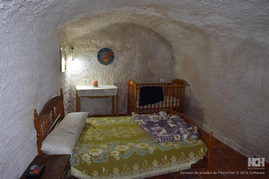 Cave house interior with rustic wooden bed, cozy decor, and arched ceiling in Cuevas del Campo, Gran.