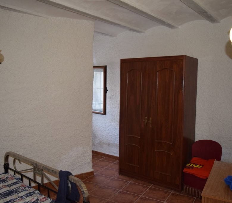 Cave house interior with wooden wardrobe, small window, and rustic furnishings in Cuevas del Campo,.