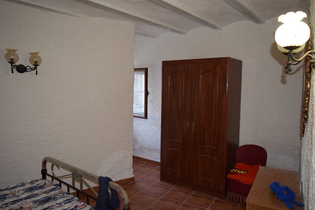 Cave house interior with wooden wardrobe, small window, and rustic furnishings in Cuevas del Campo,.