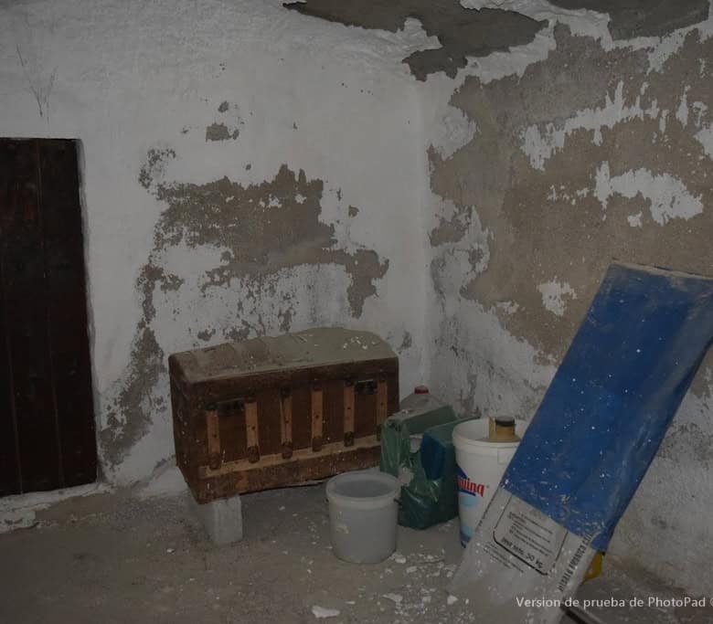 Interior of a rustic cave house in Cullar, Granada, showing aged walls and basic furnishings.