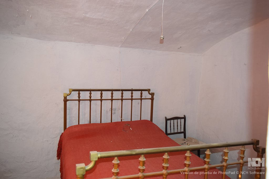 Cave house interior in Cullar, Granada with rustic bed and simple furnishings.