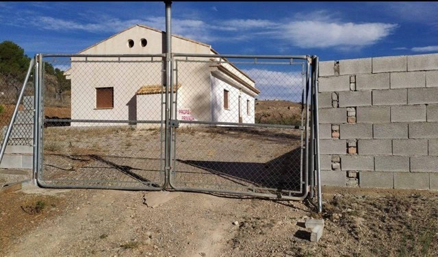 Gated entrance to rural property in Purchena, Almeria, with a white house in the background under a.
