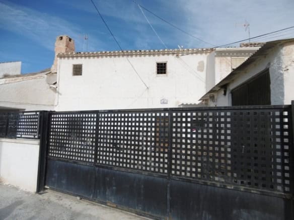Cave house exterior in El Margen, Granada with traditional white walls and a black metal gate.