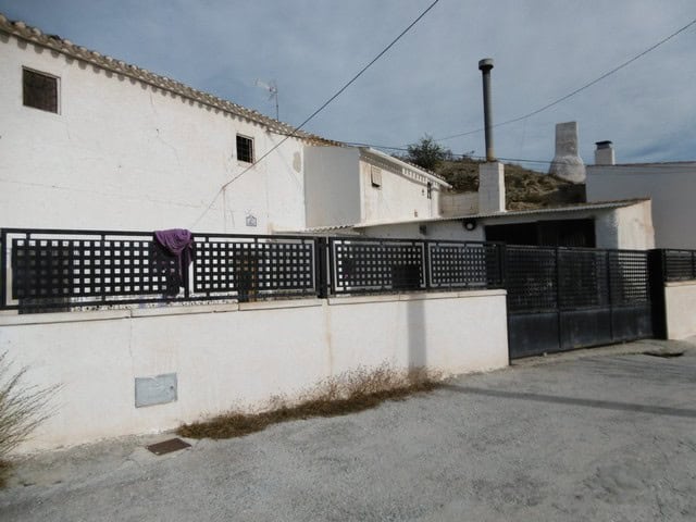 Traditional cave house with white walls and black fence in El Margen, Granada.