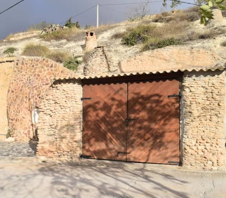 Cave house entrance in Carramaiza, Granada with rustic brick walls and wooden gate. Unique property.