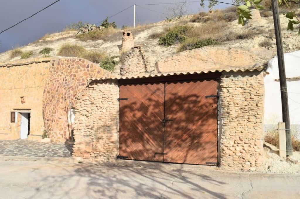 Cave house entrance in Carramaiza, Granada with rustic brick walls and wooden gate. Unique property.