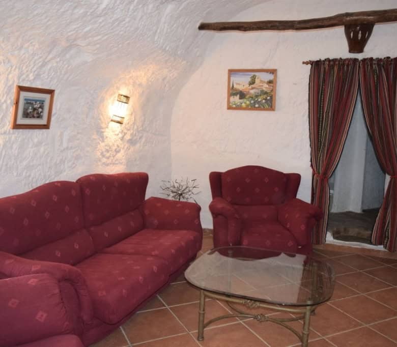 Charming cave house living room with red upholstered sofas and rustic decor in Carramaiza, Granada.