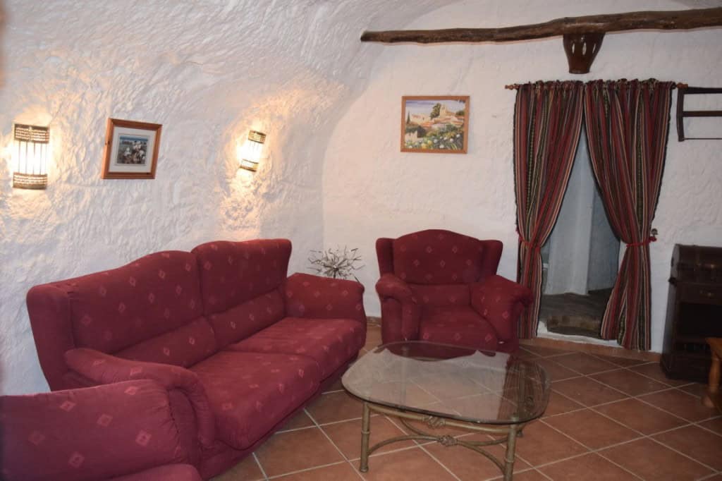 Charming cave house living room with red upholstered sofas and rustic decor in Carramaiza, Granada.