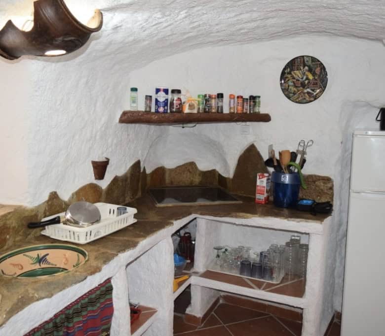 Cave house kitchen with rustic stone countertops, shelves, and traditional decor in Carramaiza, Gran.