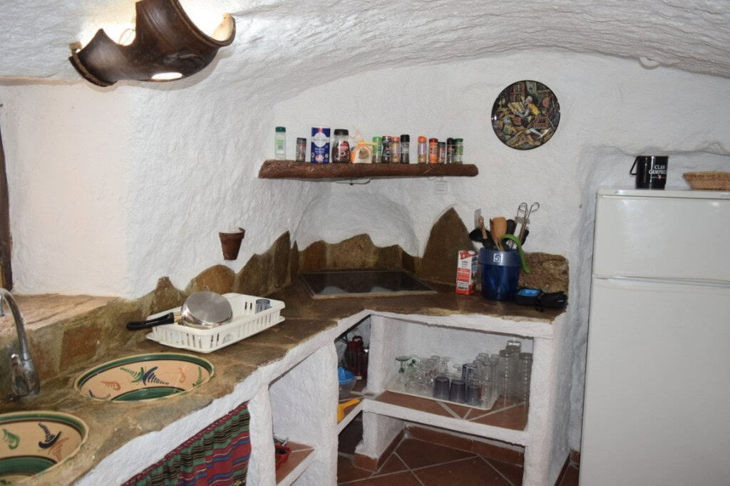 Cave house kitchen with rustic stone countertops, shelves, and traditional decor in Carramaiza, Gran.