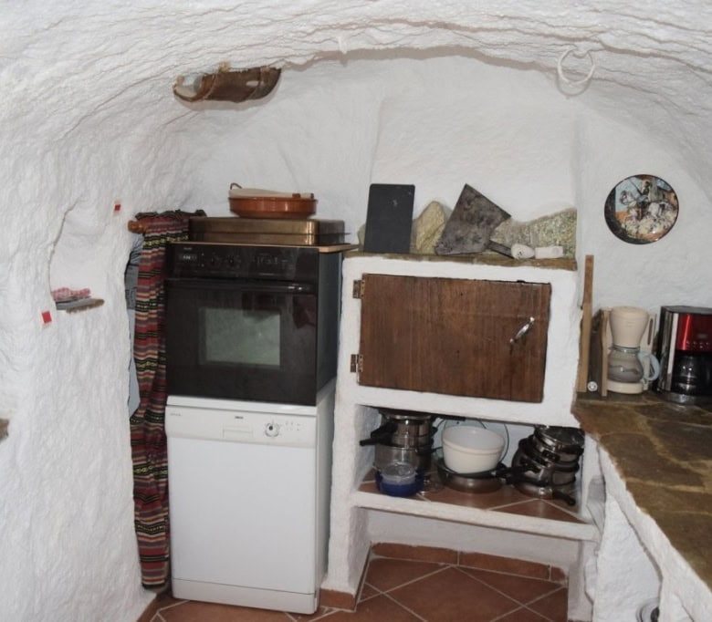 Charming cave house interior in Carramaiza, Granada, featuring rustic kitchen with oven, shelves, an.