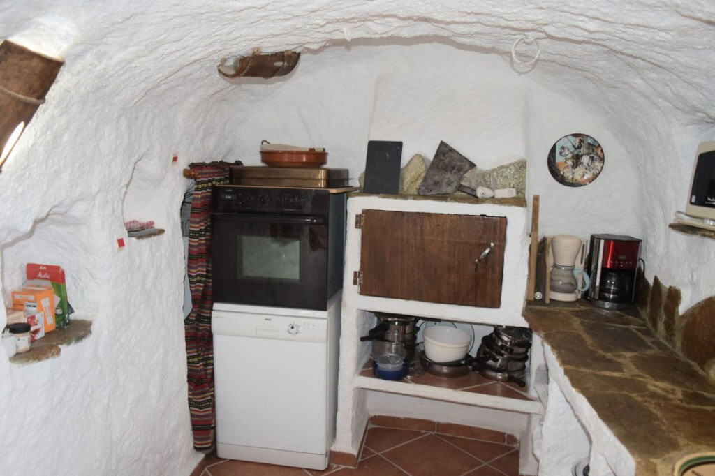 Charming cave house interior in Carramaiza, Granada, featuring rustic kitchen with oven, shelves, an.