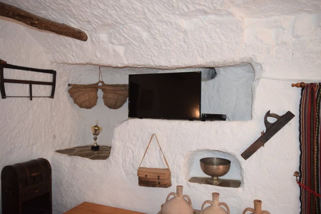 Cave house interior with traditional decor in Carramaiza, Granada, featuring a TV, rustic shelves, a.