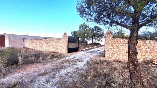 Rural property entrance with stone wall and dirt path in Freila, Granada.