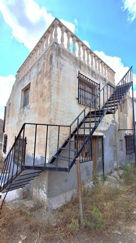 Rural property in Albox with exterior staircase and weathered walls, set against a bright blue sky.