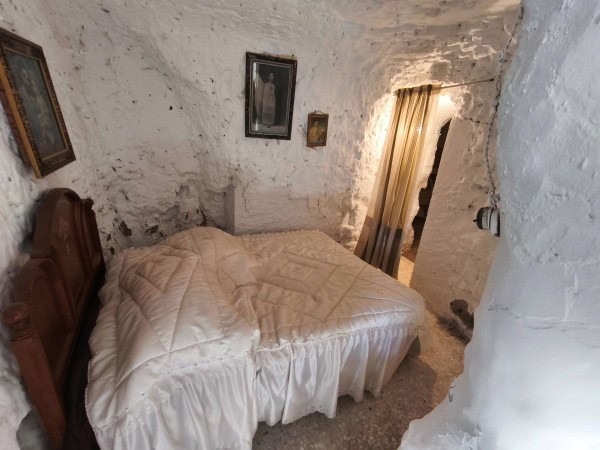 Charming cave house interior in Baza, Granada, featuring rustic stone walls and cozy bedroom ambianc.