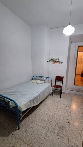 Interior of a simple bedroom in Seron, Almeria, with a metal bed, a wooden chair, and basic furnishi.