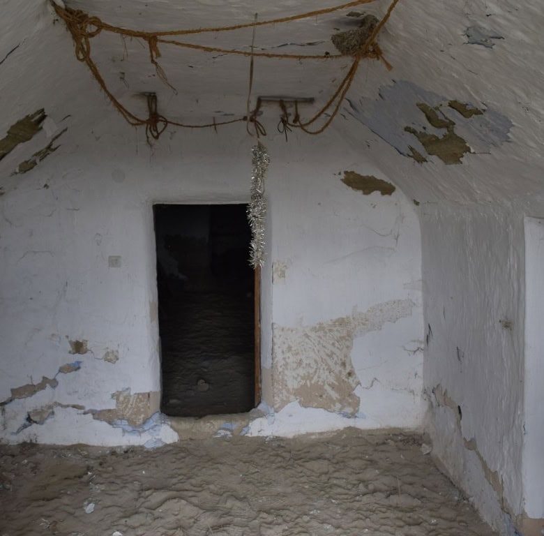 Interior view of a rustic cave house in Benamaurel, Granada, showing aged whitewashed walls and a si.