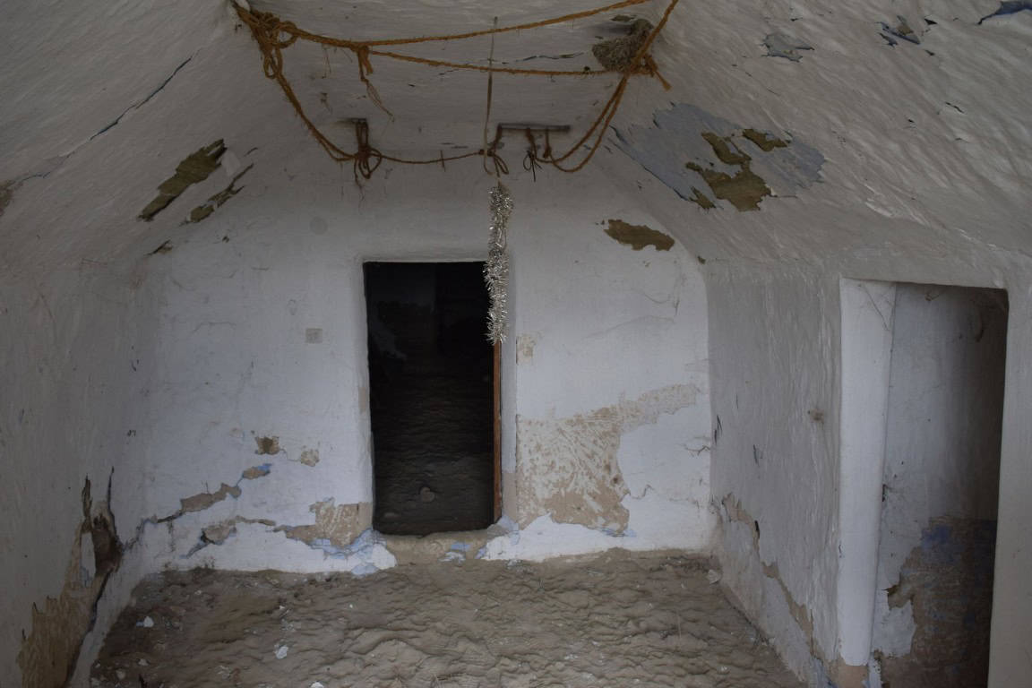 Interior view of a rustic cave house in Benamaurel, Granada, showing aged whitewashed walls and a si.